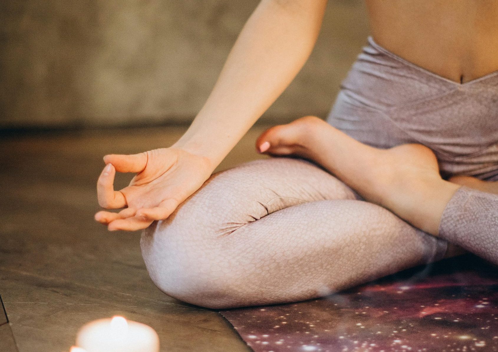 A woman practicing yoga indoors in lotus pose with candles creating a calming atmosphere.