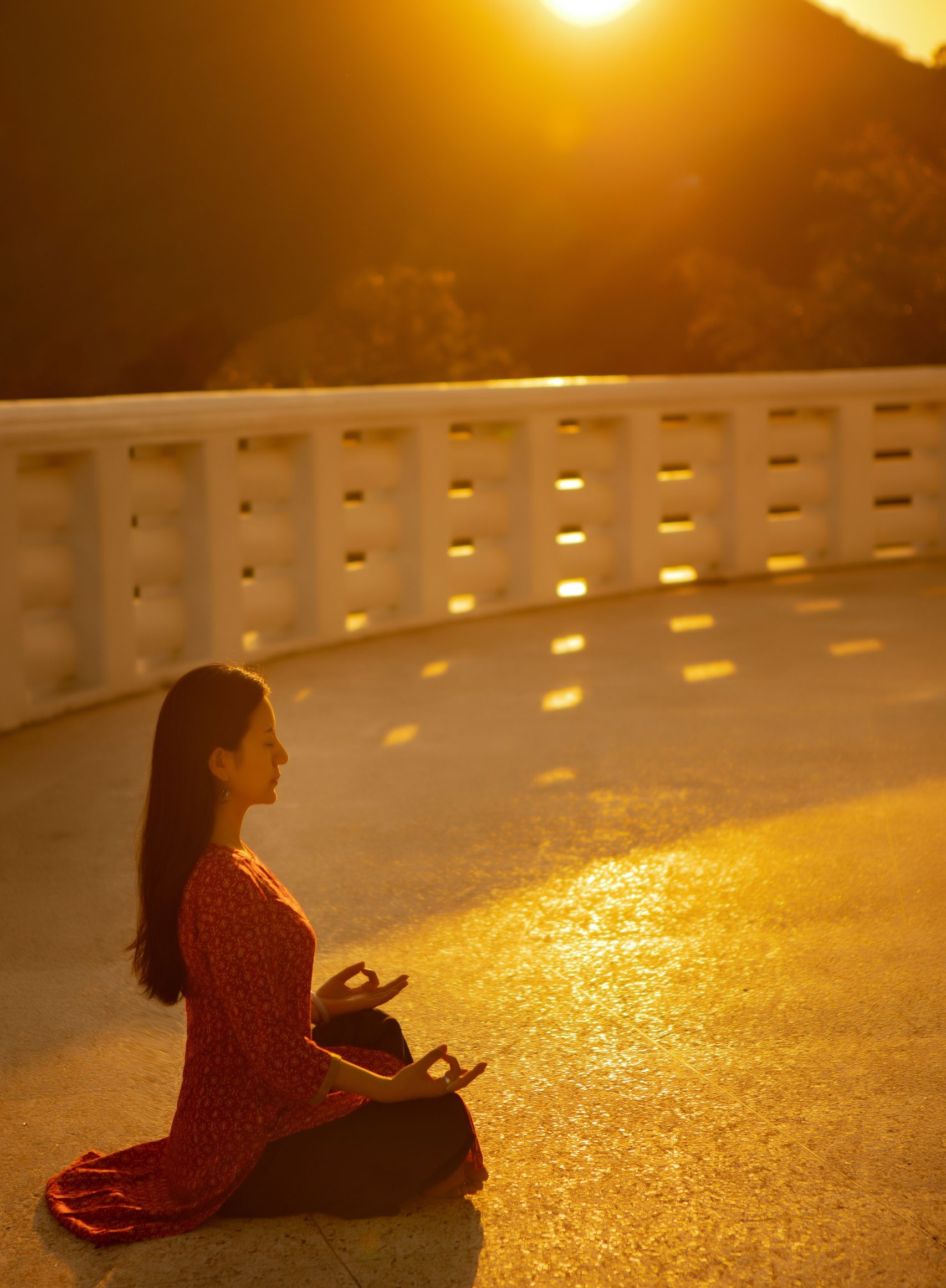 A woman practices yoga meditation in a serene outdoor setting during a golden sunset.