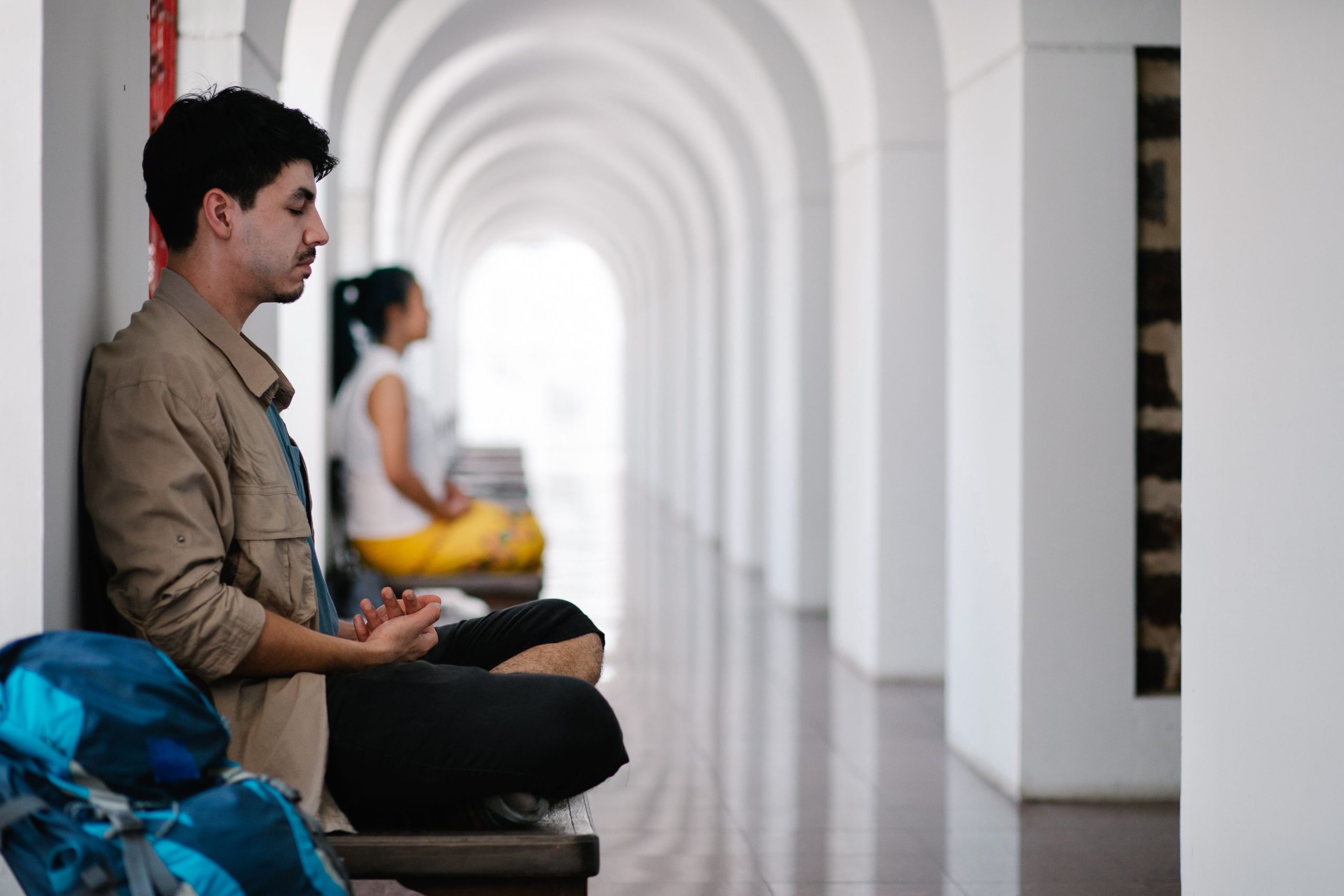 Man and woman meditate in a serene corridor, emphasizing relaxation.